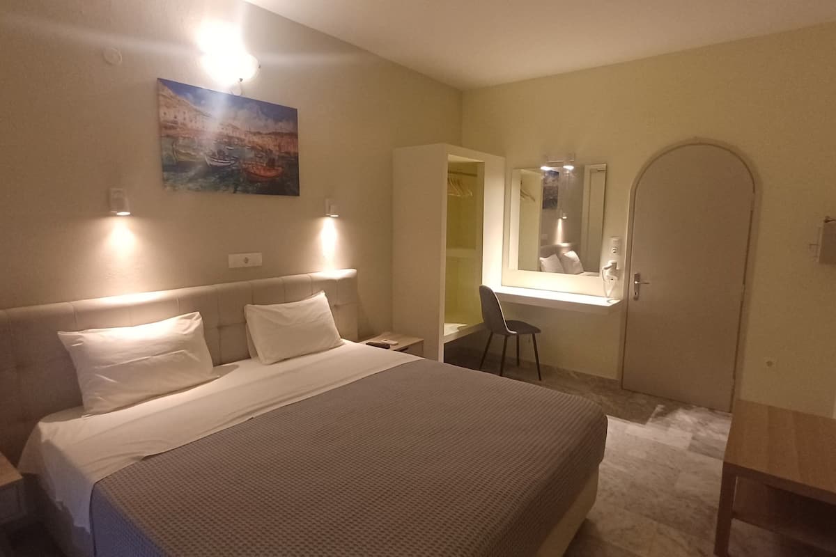 Une chambre d’hôtel comprenant un lit, des tables de chevet, un bureau avec une chaise, un miroir et un tableau au mur.