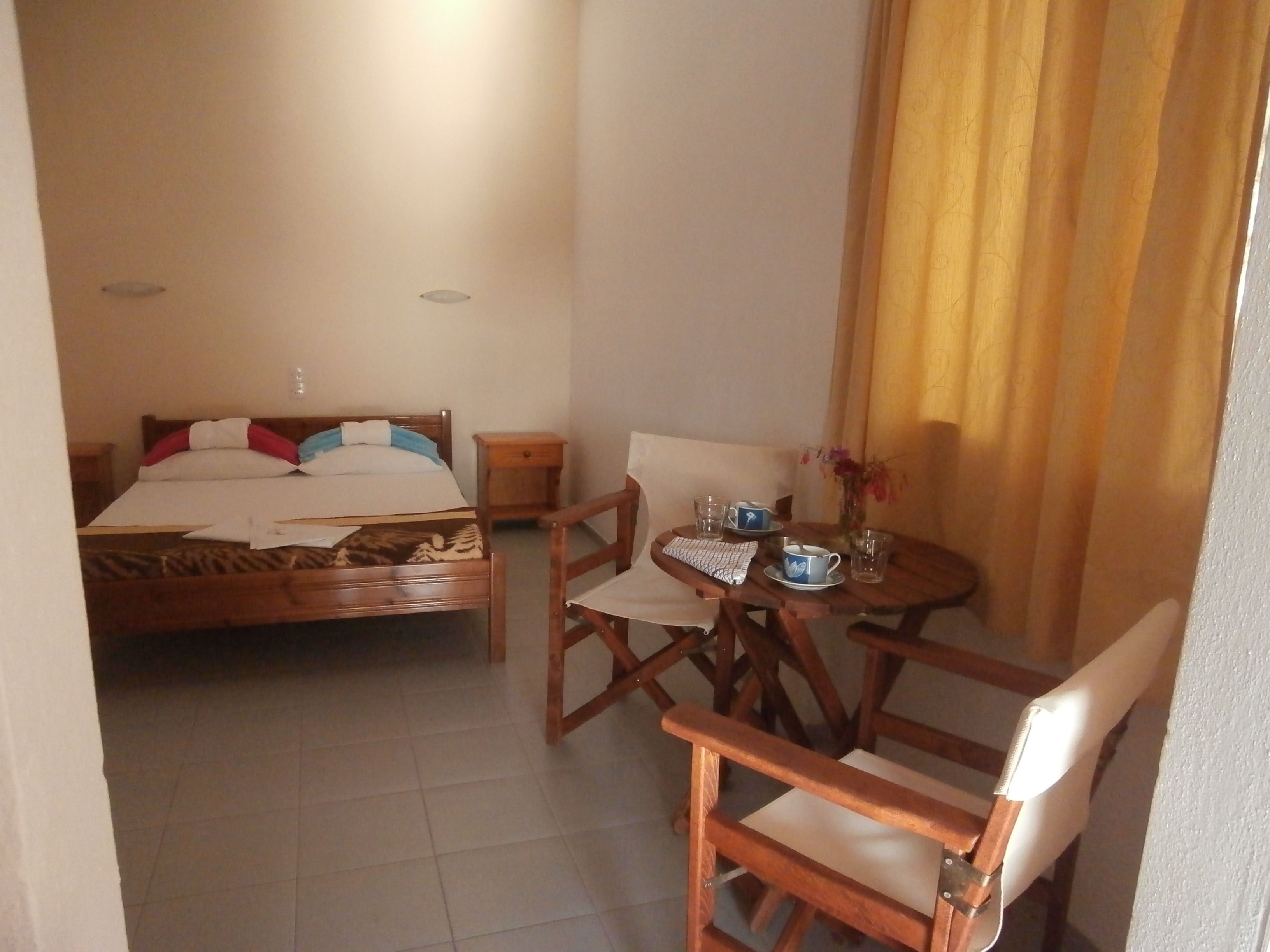 A hotel room with a bed, a small table with a chair, and a window with curtains.