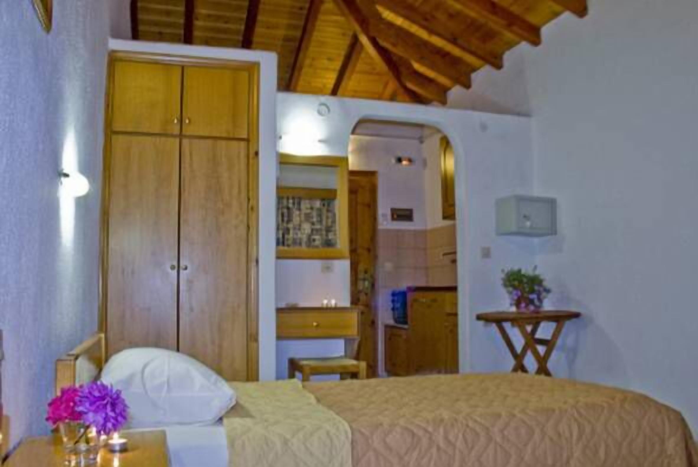 A bedroom with a bed, wooden wardrobe, bedside table with flowers, and a small table with a plant.