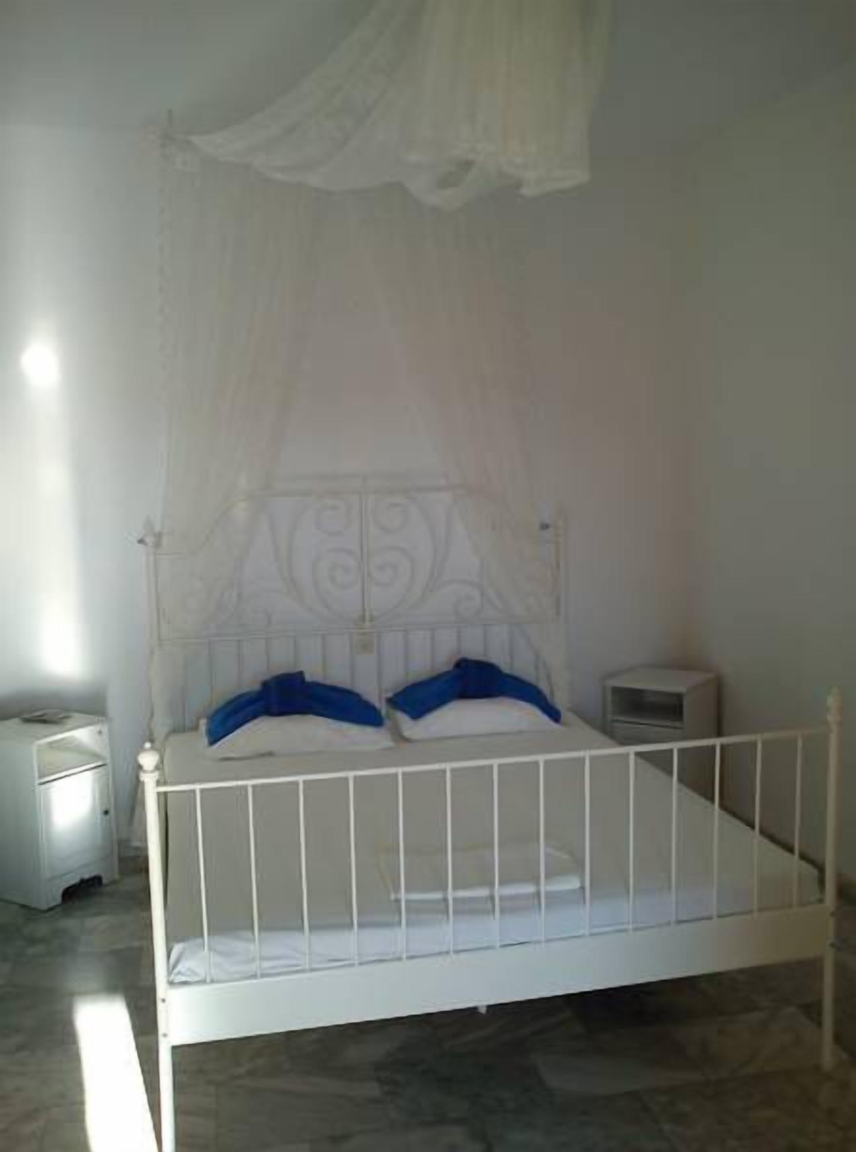 Un lit en métal blanc avec un baldaquin, une table de chevet et une petite table de nuit.