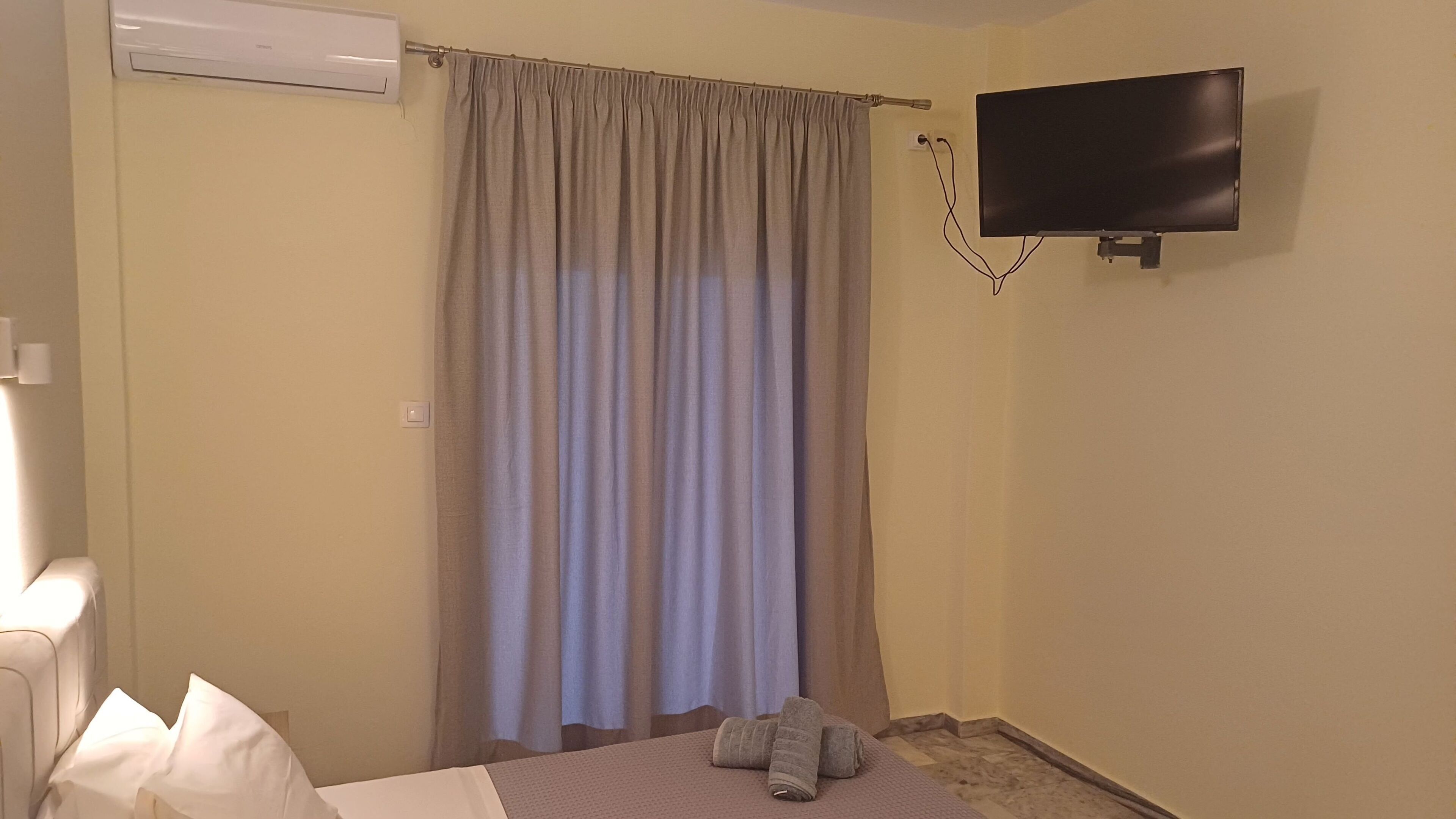 Een hotelkamer met een bed, een aan de muur bevestigde televisie en een gordijn.