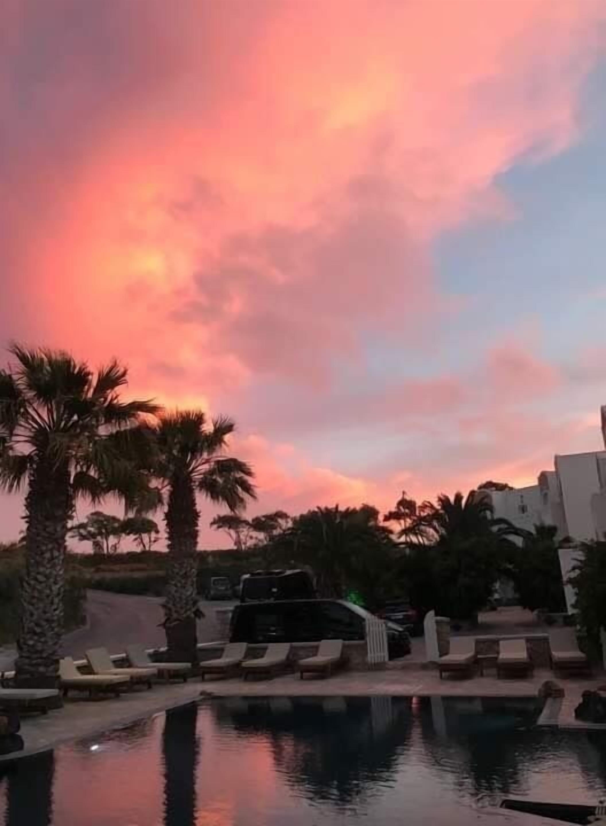 Zona de piscina con sillas de descanso y una piscina, rodeada de palmeras y edificios.