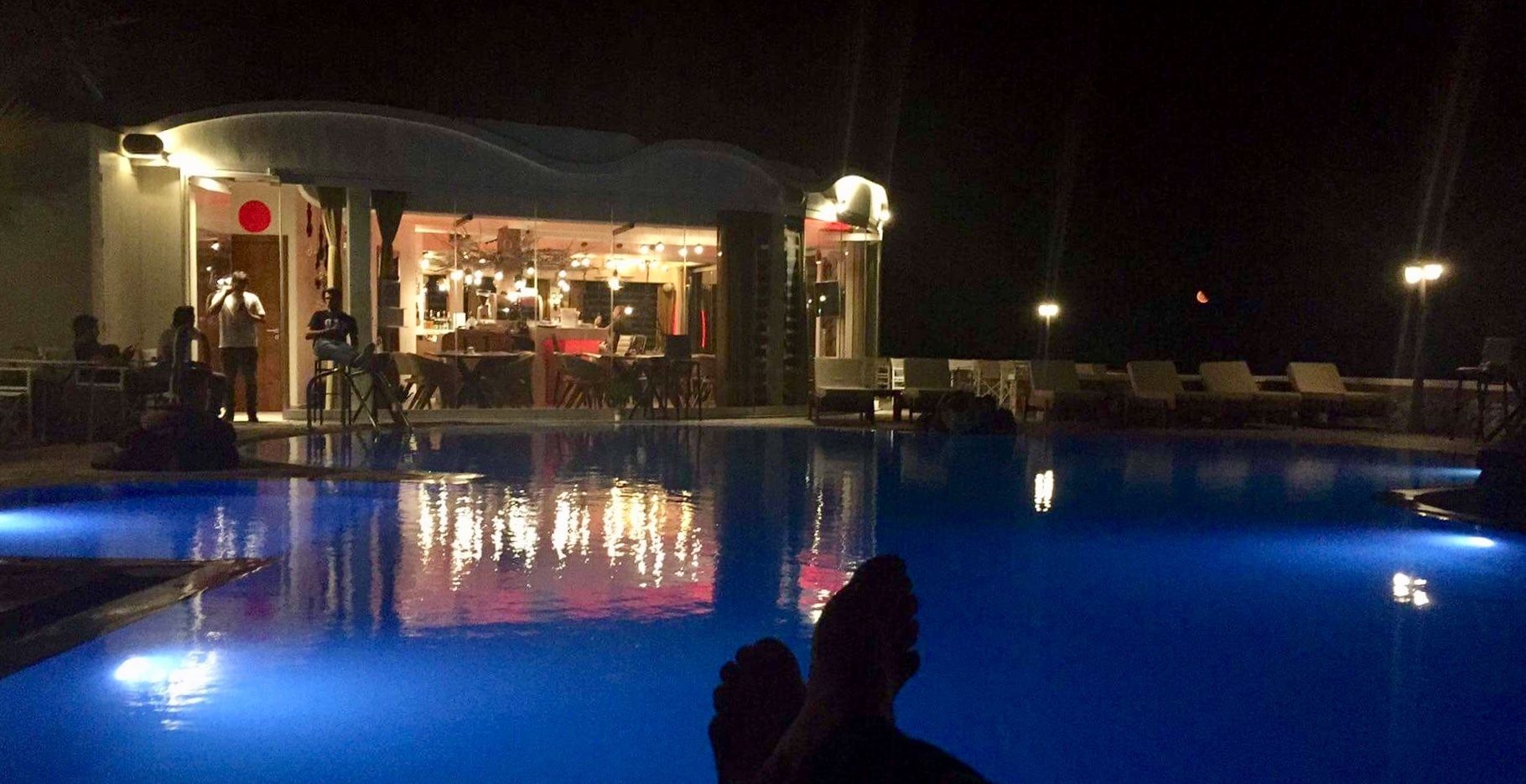 Een zwembadgebied bij nacht, met ligbedden en een bar in de verte.