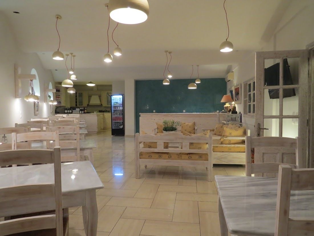 Un comedor amplio con mesas y sillas de madera, un espacio de estar central con un sofá y cojines, e iluminación colgante.