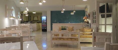 Un comedor amplio con mesas y sillas de madera, un espacio de estar central con un sofá y cojines, e iluminación colgante.