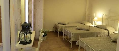 Un dormitorio con tres camas, una mesita de noche con lámpara, una pequeña mesa con farol y un armario blanco.
