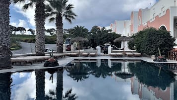 Relax by the serene pool surrounded by palm trees and lounge chairs, with a tranquil bridge connecting the space.
