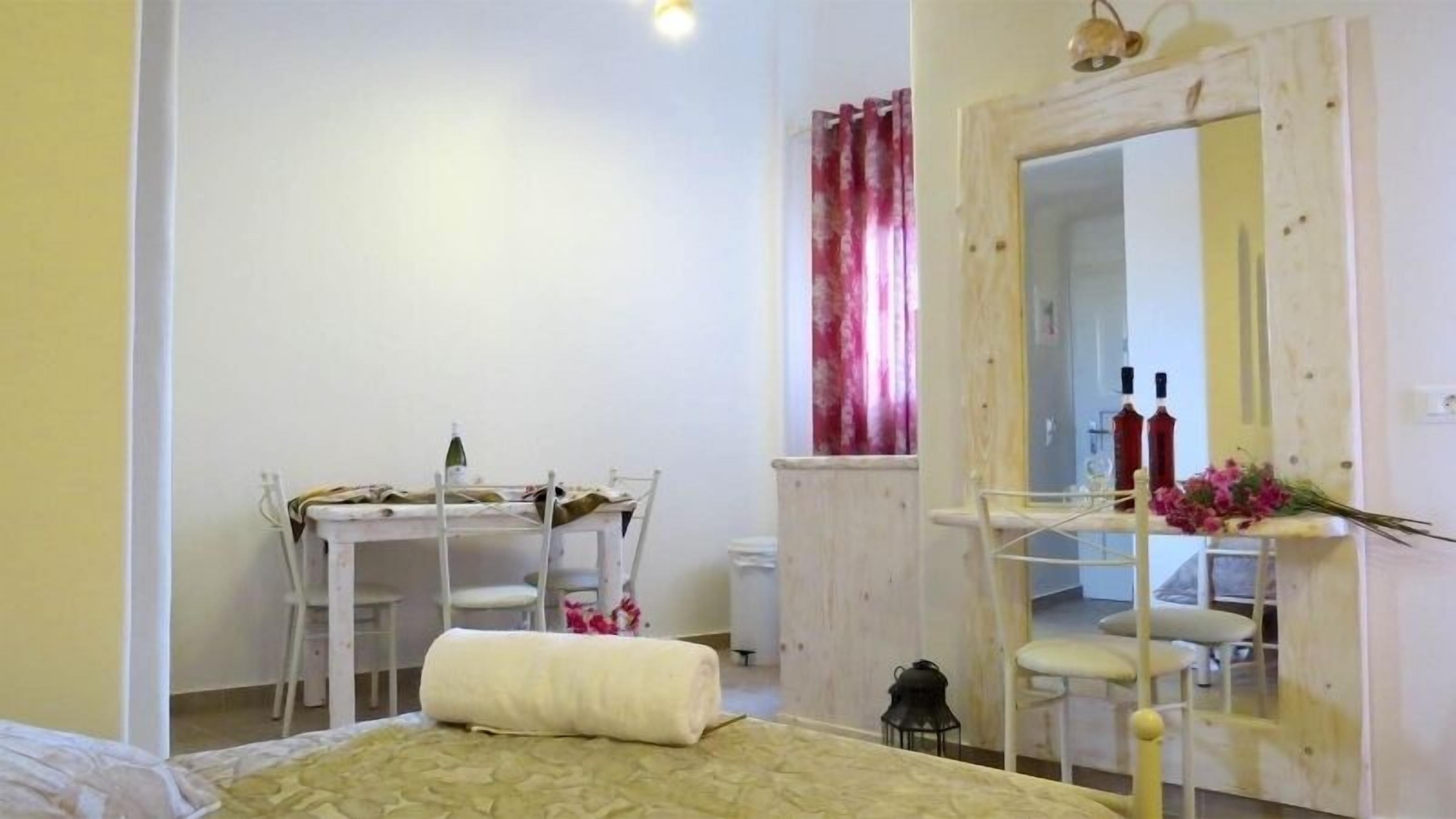Un dormitorio con cama, escritorio y silla. Hay un espejo en la pared y una ventana con cortinas.