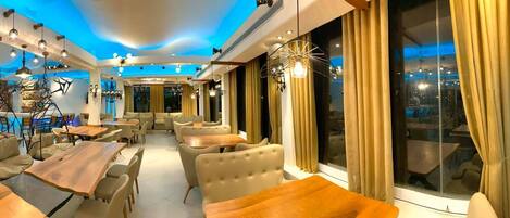 Un interior de restaurante moderno con varias zonas de estar, incluidas mesas y cabinas, y una barra visible al fondo.