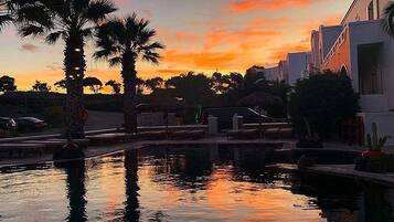 Zonsondergang met palmbomen en een zwembad dat de lucht weerspiegelt.
