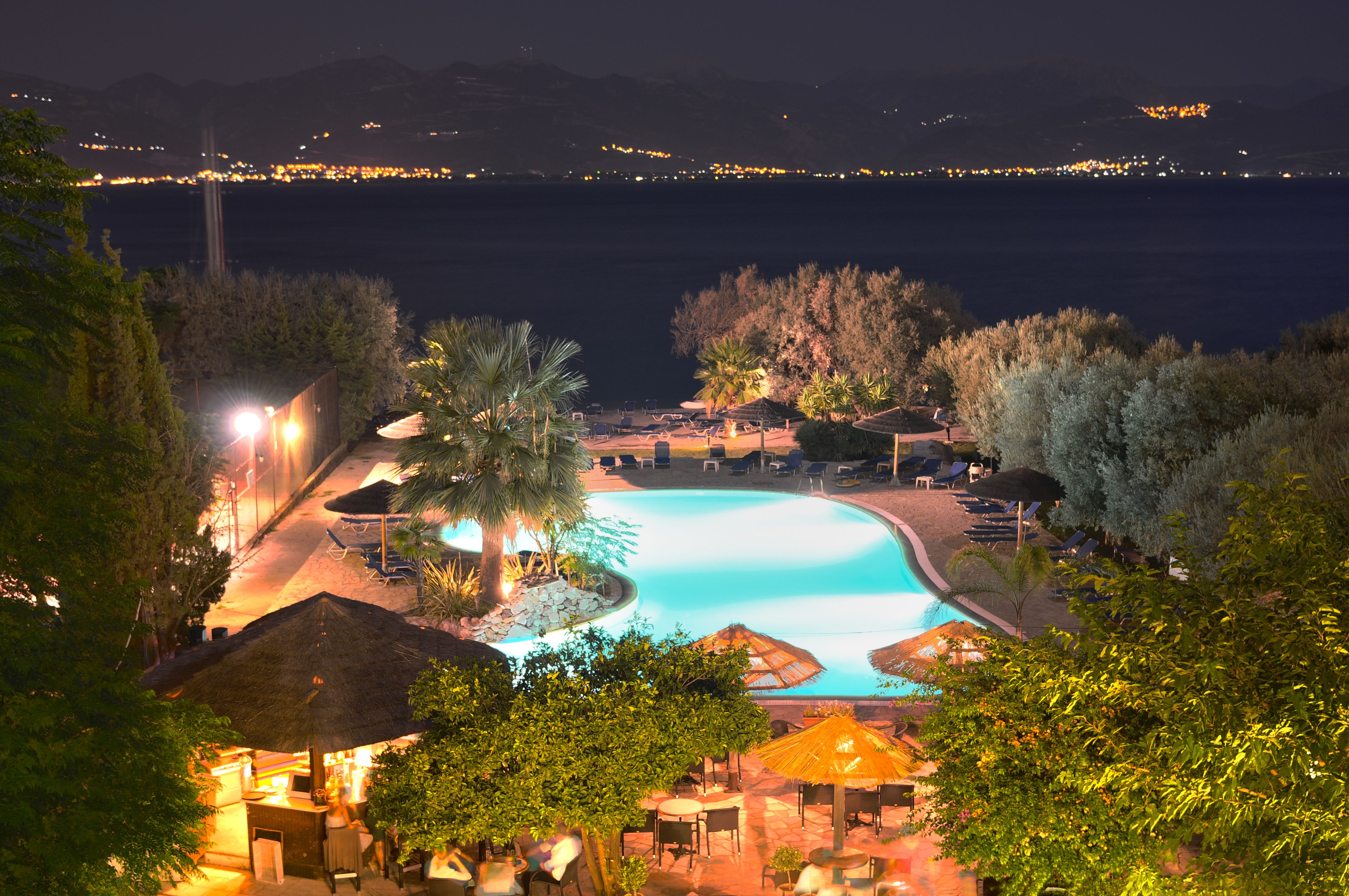 A nighttime view of a resort with a swimming pool, lounge chairs, and umbrellas.