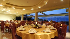 Un comedor con mesas redondas dispuestas para una comida, ventanas amplias que ofrecen vistas a las montañas y un diseño de techo moderno.