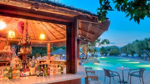Un área de bar con techo de paja, una piscina y asientos al aire libre.
