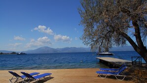 Una terraza de madera con sillones de descanso azules con vistas a un cuerpo de agua, un muelle y montañas al fondo.