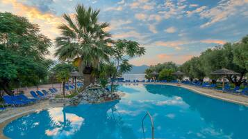 A pool area with blue lounge chairs, a stone structure, and palm trees.