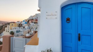 A blue door with a sign for Chroma Suites, white buildings, and a view of a hillside. - Chroma Suites (Santorini)
