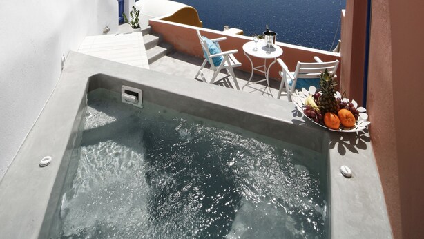 A balcony with a hot tub, white and blue furniture, and a table with fruit. - Chroma Suites (Santorini)