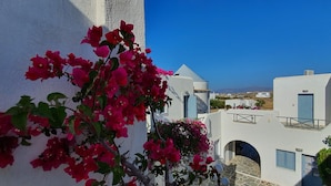 A white building with blue shutters and a balcony, surrounded by bougainvillea flowers. - Teoria Paros | Matsas Windmill (Paros)