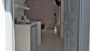 A narrow hallway with a kitchen area on the left, featuring a sink and cabinets. An arched doorway leads to another room. - Teoria Paros | Matsas Windmill (Paros)