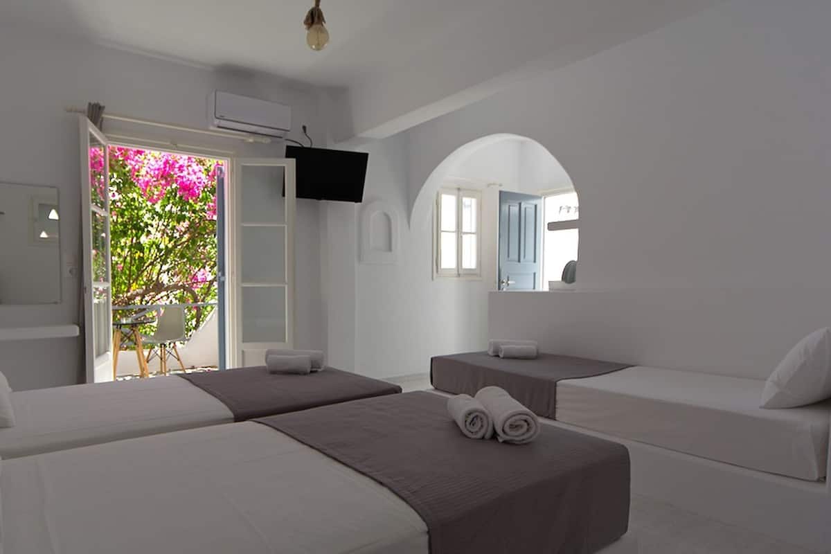 A hotel room with two beds, a small table, a chair, a TV, and a bathroom with a mirror.