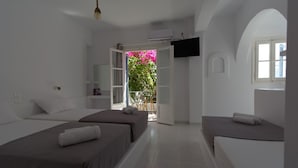 A hotel room with two beds, a TV mounted on the wall, and a view of a garden through an open door. - Teoria Paros | Matsas Windmill (Paros)