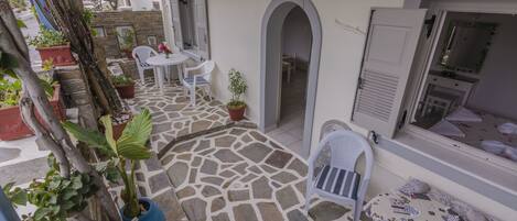 Un patio con pavimento in pietra, arredi bianchi, piante in vaso e un arco che conduce a una stanza con una toeletta e uno specchio.