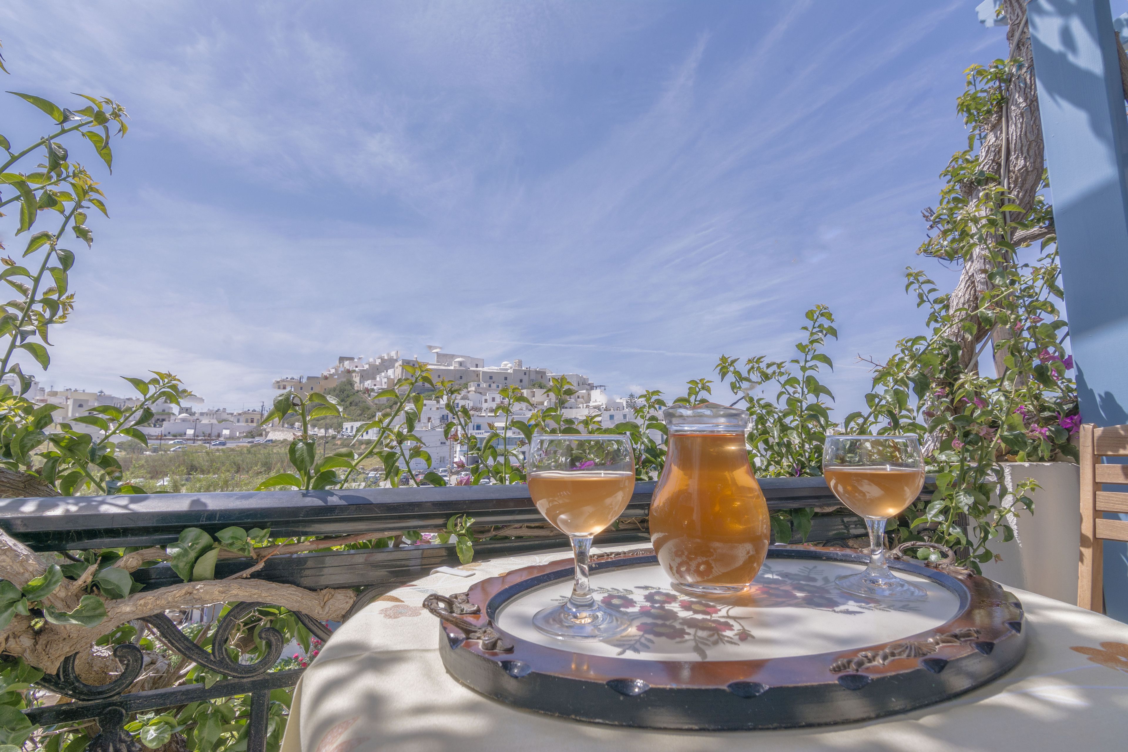 Ein Tisch mit zwei Gläsern eines hellen Getränks und einer Karaffe, vor der Kulisse einer Stadtlandschaft und Grünflächen.