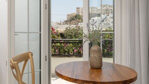 A round wooden table with two chairs, a hanging light fixture, and a view through a glass door to an outdoor balcony with flowers and buildings. - Pension Sofi (Naxos)