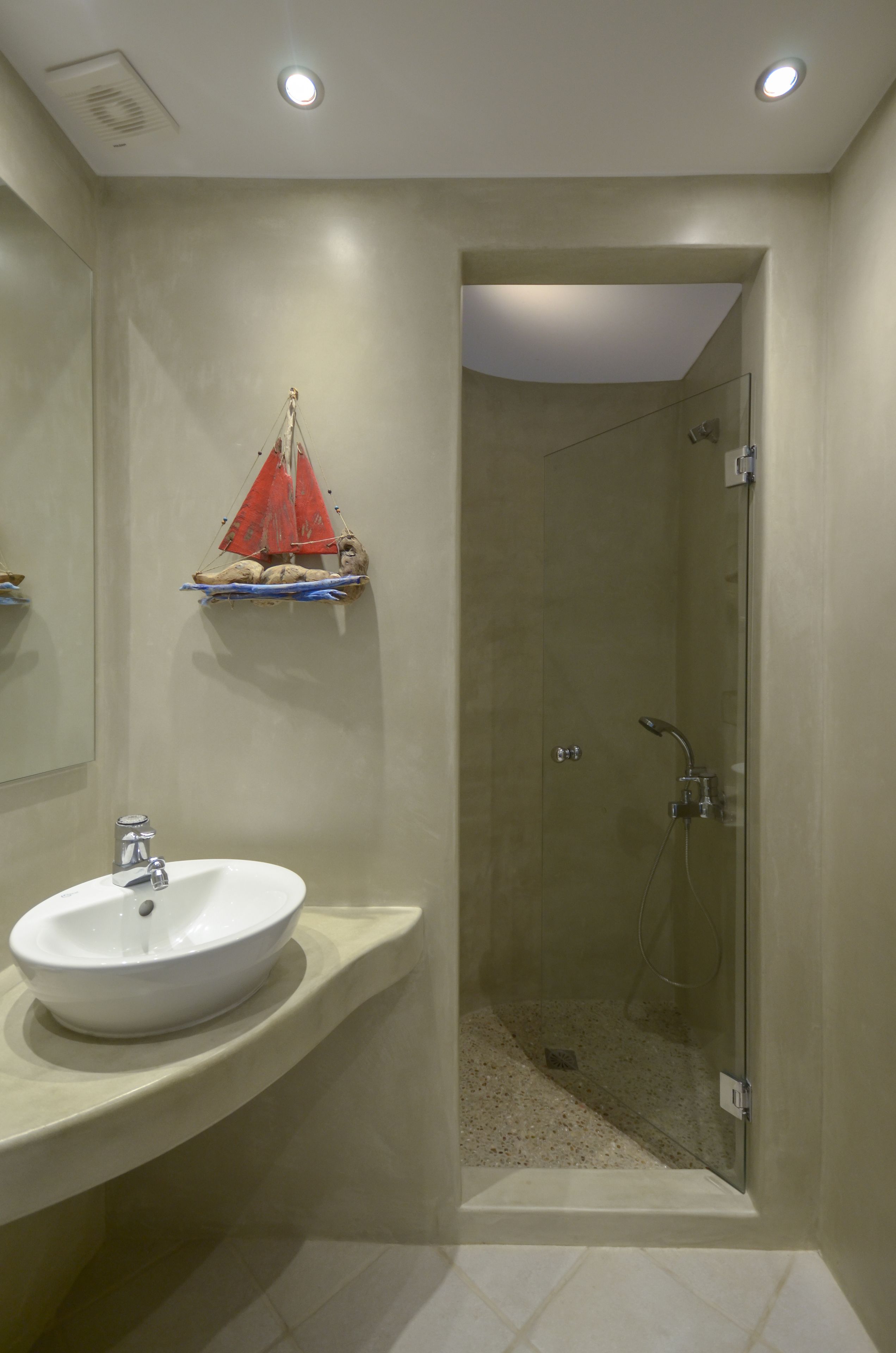 Une salle de bain avec un lavabo blanc, une douche en verre et un objet décoratif rouge accroché au mur.