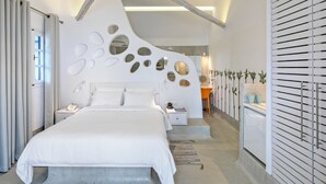 A modern bedroom with a large bed, a bedside table, a nightstand, a desk, and a built-in wardrobe. - Kouros Village Hotel - Adults Only (Santorini)