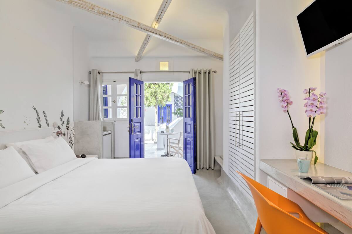 Habitación de hotel con cama, escritorio, silla, televisor y vistas al exterior.