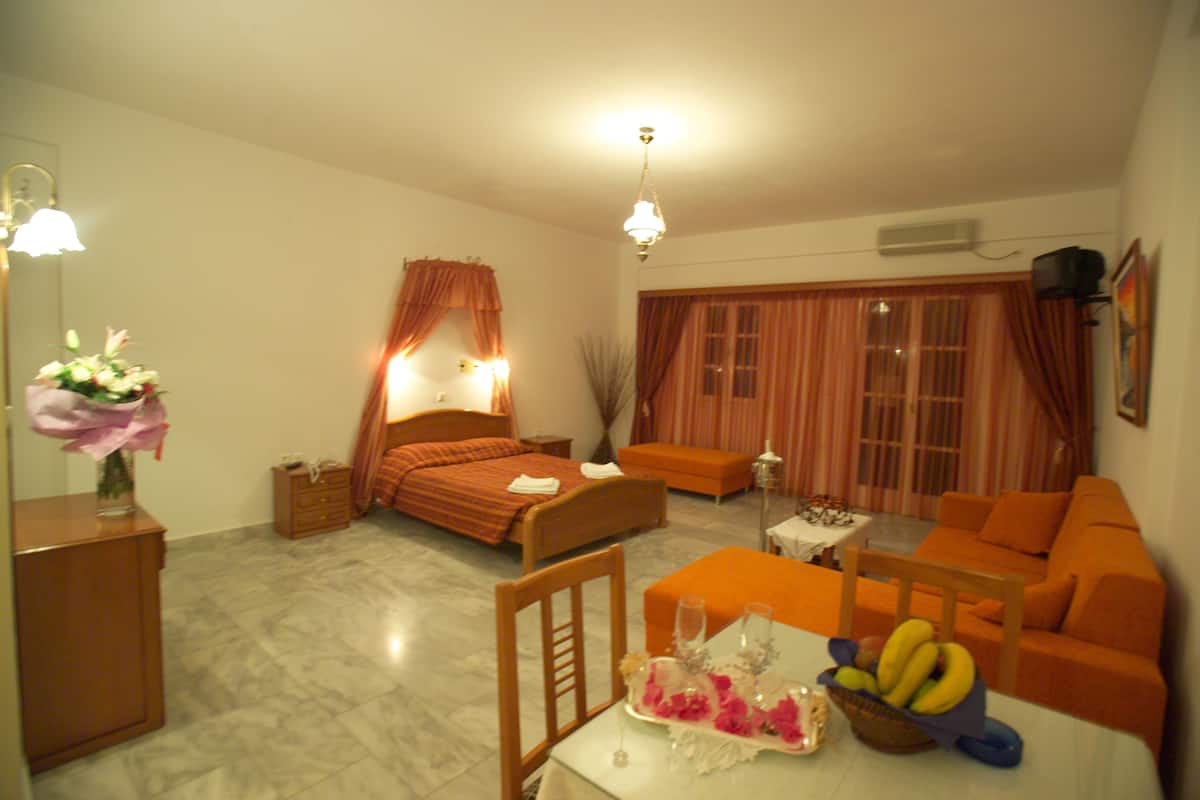 Ein Hotelzimmer mit Bett, Sofa, Esstisch mit Obstkorb und einem kleinen Tisch mit Blumenvase.