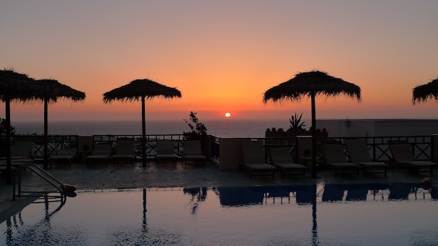 Zona junto a la piscina con sillones de descanso y sombrillas, con vista al mar al atardecer.