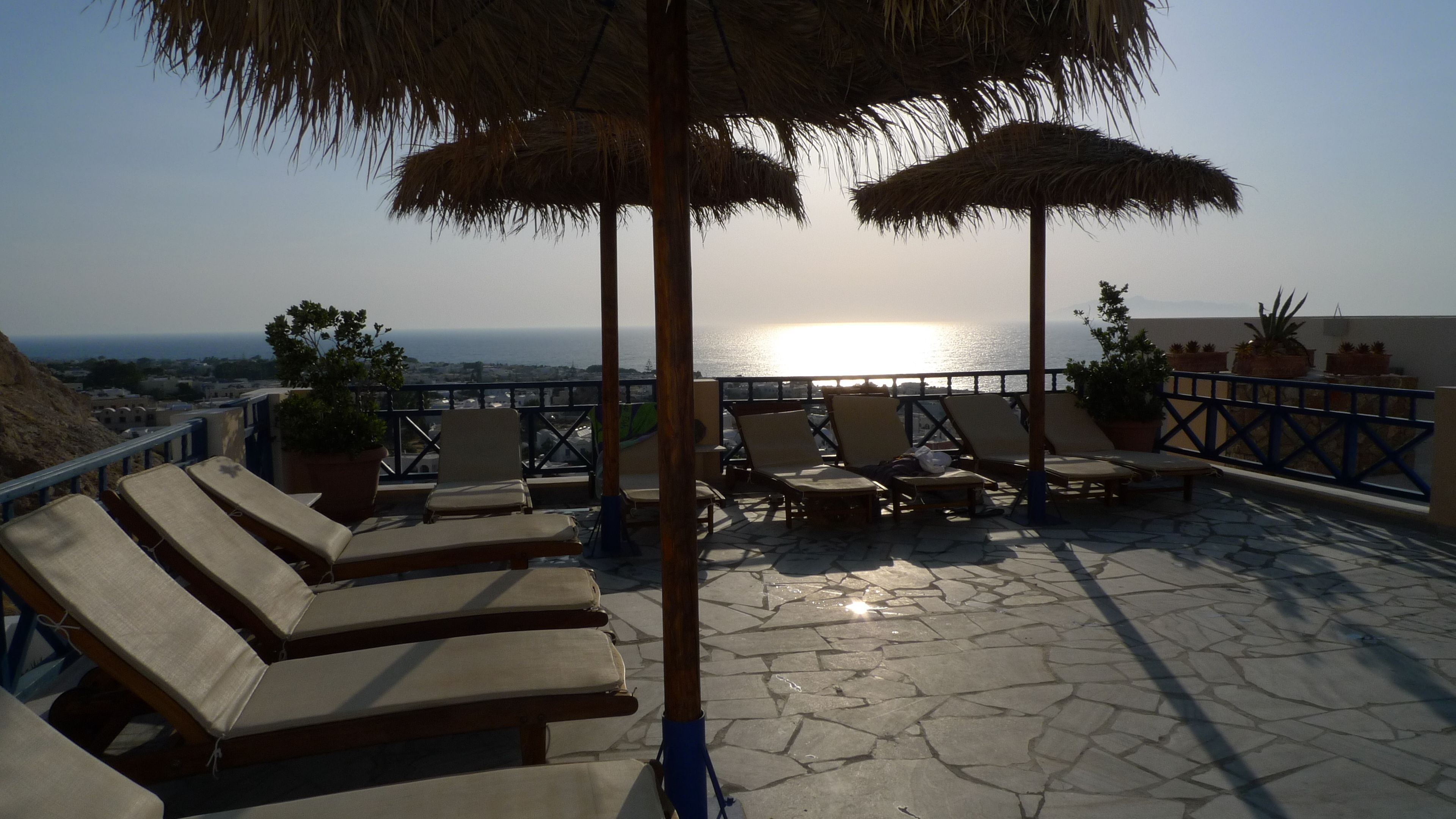 A rooftop terrace with lounge chairs and umbrellas, overlooking a coastal view.
