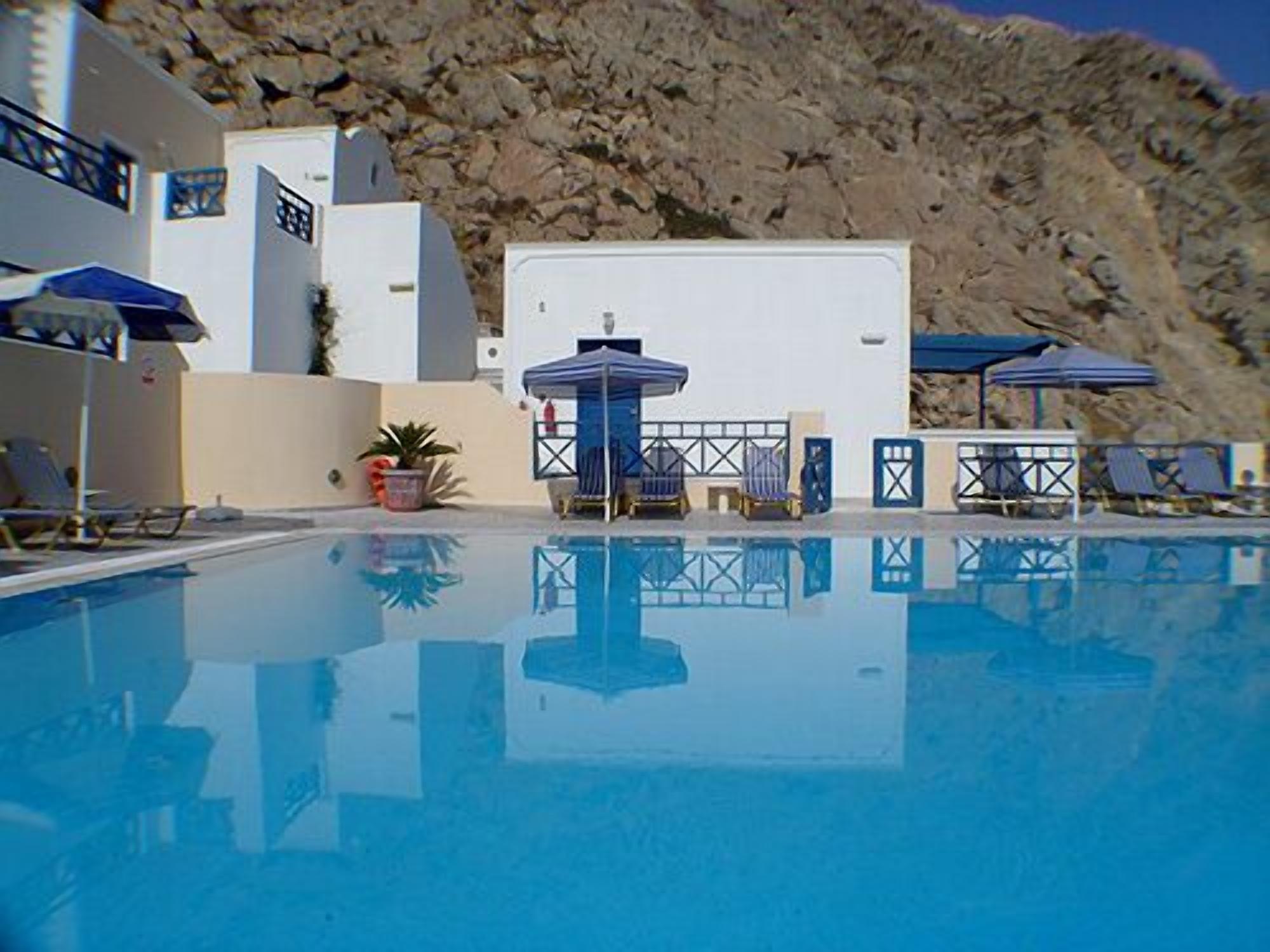 A swimming pool with lounge chairs and umbrellas, surrounded by a mountainous landscape.