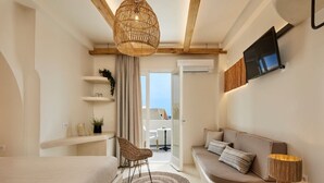 A modern bedroom with a bed, a sofa, a chair, a TV, and a window. - Hermes Hotel (Santorini)