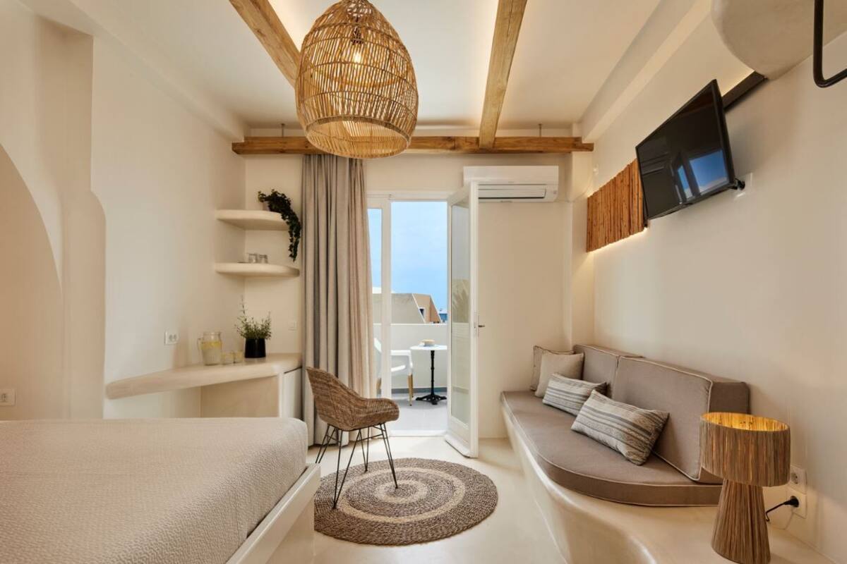 A modern bedroom with a bed, a sofa, a chair, a TV, and a window.