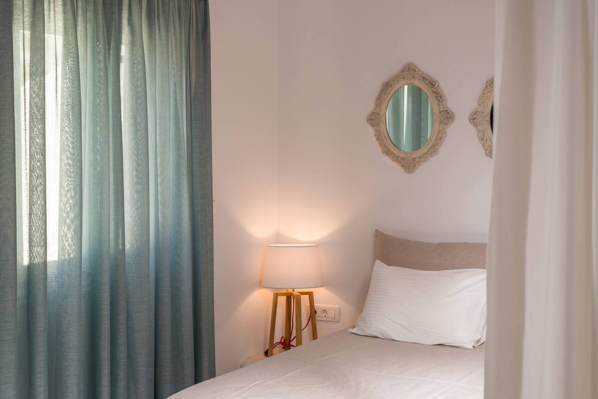 A hotel room with a bed, a nightstand with a lamp, and two wall mirrors.