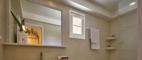 A bathroom with a large mirror, a sink, a shower, and a small shelf with toiletries.