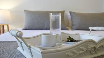 Una bandeja blanca con una taza de café y un vaso de agua sobre una cama con almohadillas grises.