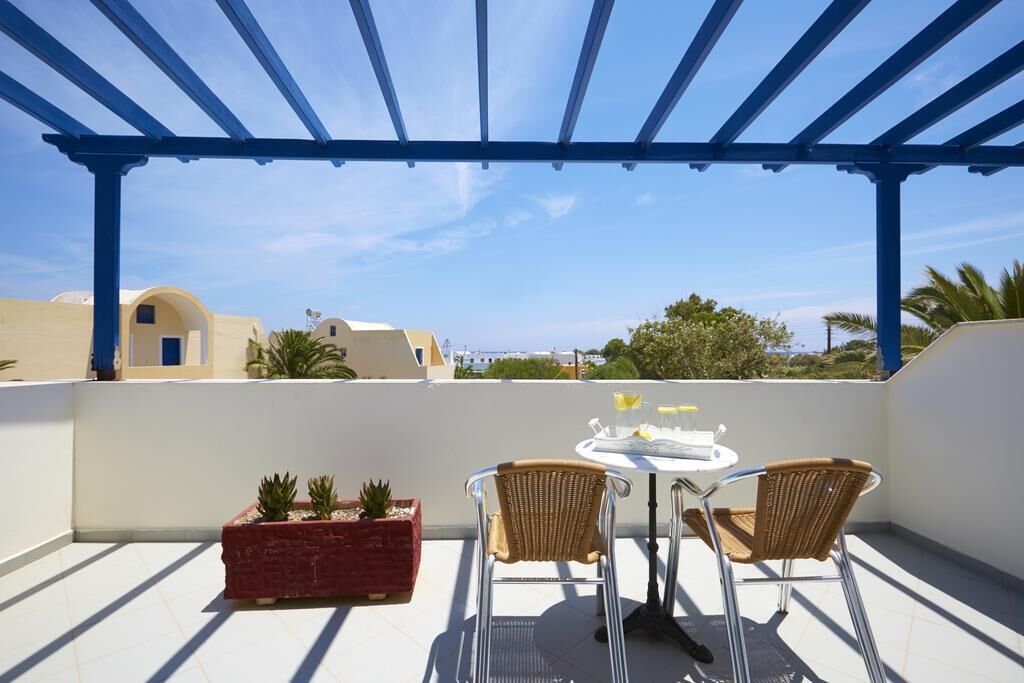 A balcony with a blue pergola, two wicker chairs, a small table with a glass, and potted plants.