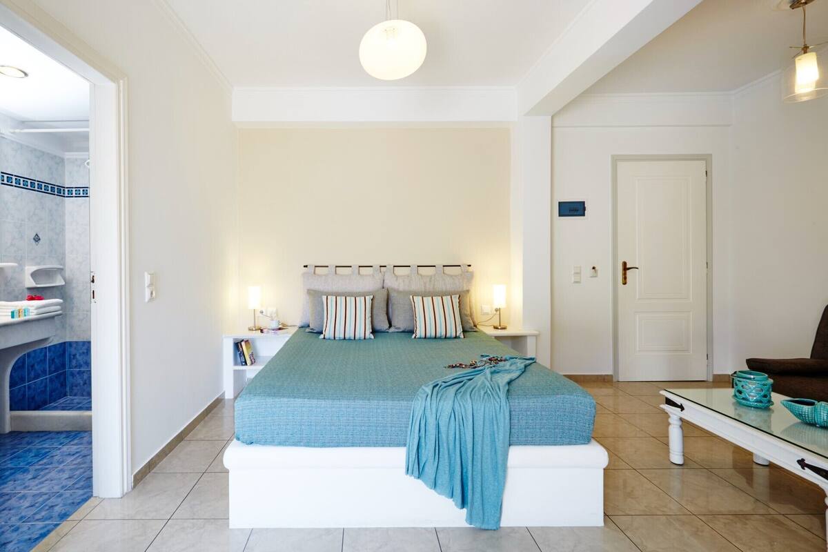 A bedroom with a bed, bedside tables, a nightstand, a door, and a bathroom visible through an open door.