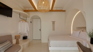 A bedroom with a bed, a sofa, a hanging light fixture, and a door. - Hermes Hotel (Santorini)