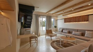 A modern living room with a sofa, chairs, a coffee table, and a staircase. - Hermes Hotel (Santorini)