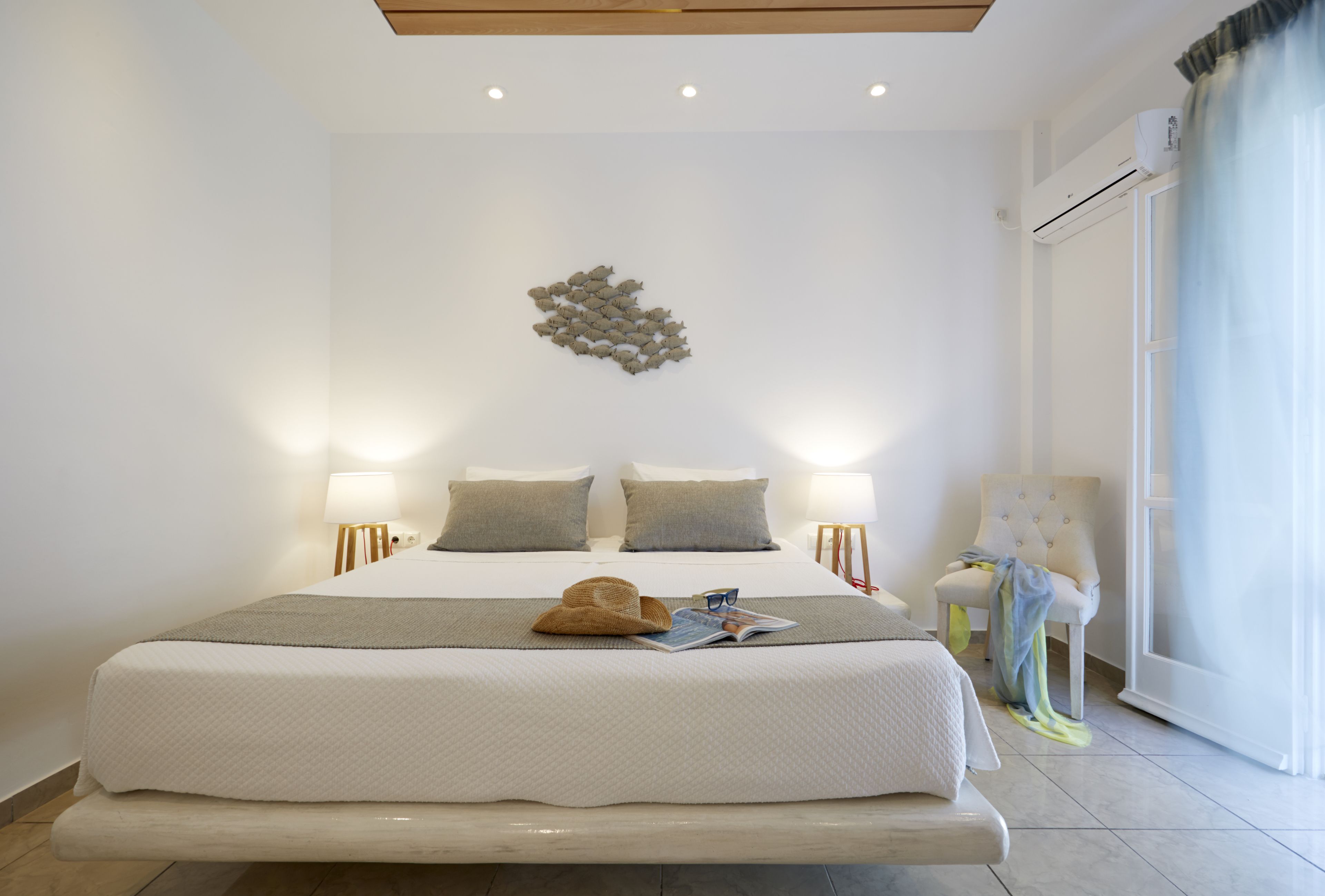 A modern bedroom with a large bed, two bedside lamps, a decorative wall piece, and a chair by the window.