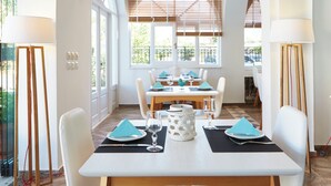 A dining area with a table set for four, large windows, and a view of the outdoors. - Hermes Hotel (Santorini)