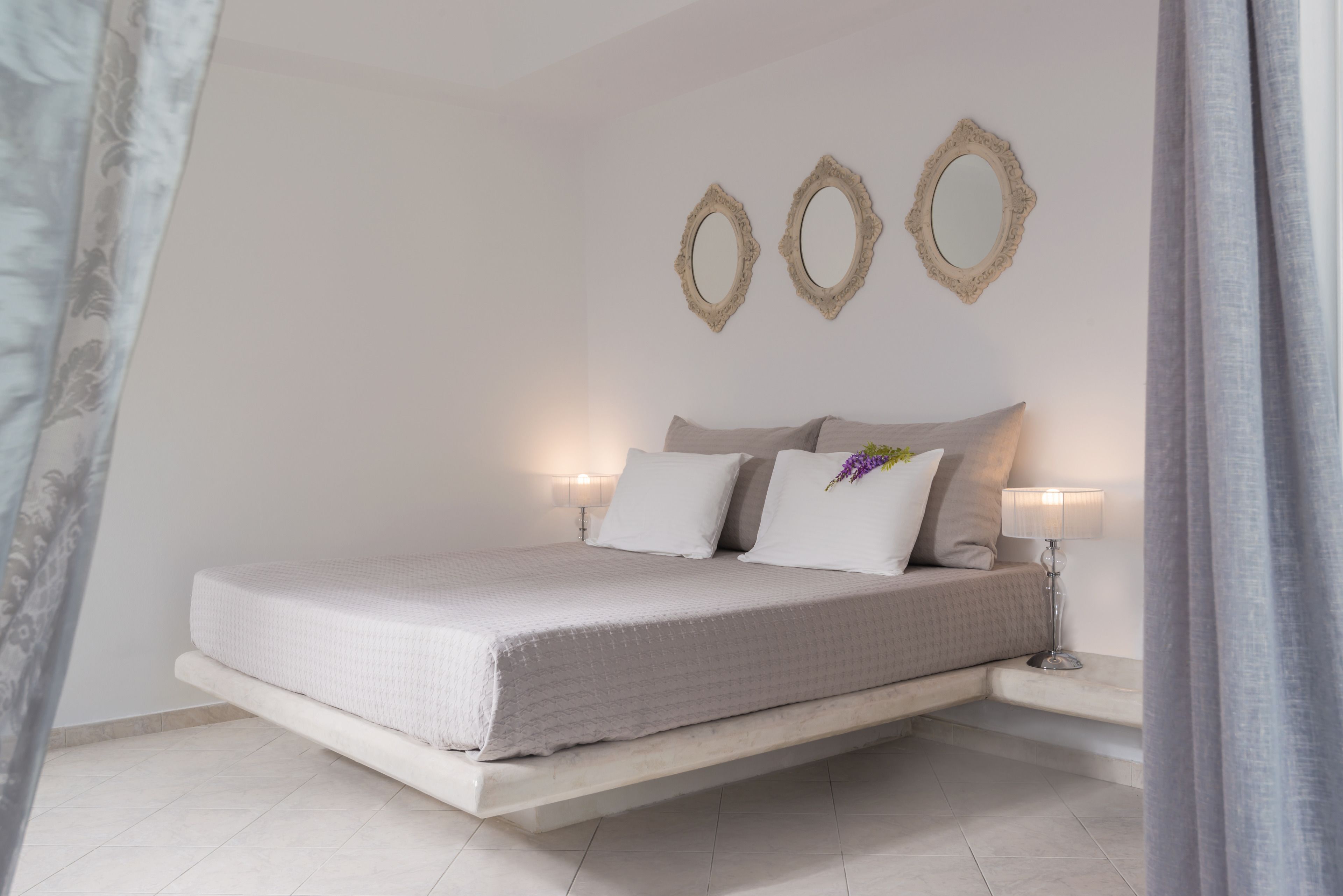 Une chambre à coucher au style minimaliste, avec un lit, des lampes de chevet et des miroirs décoratifs sur les murs.