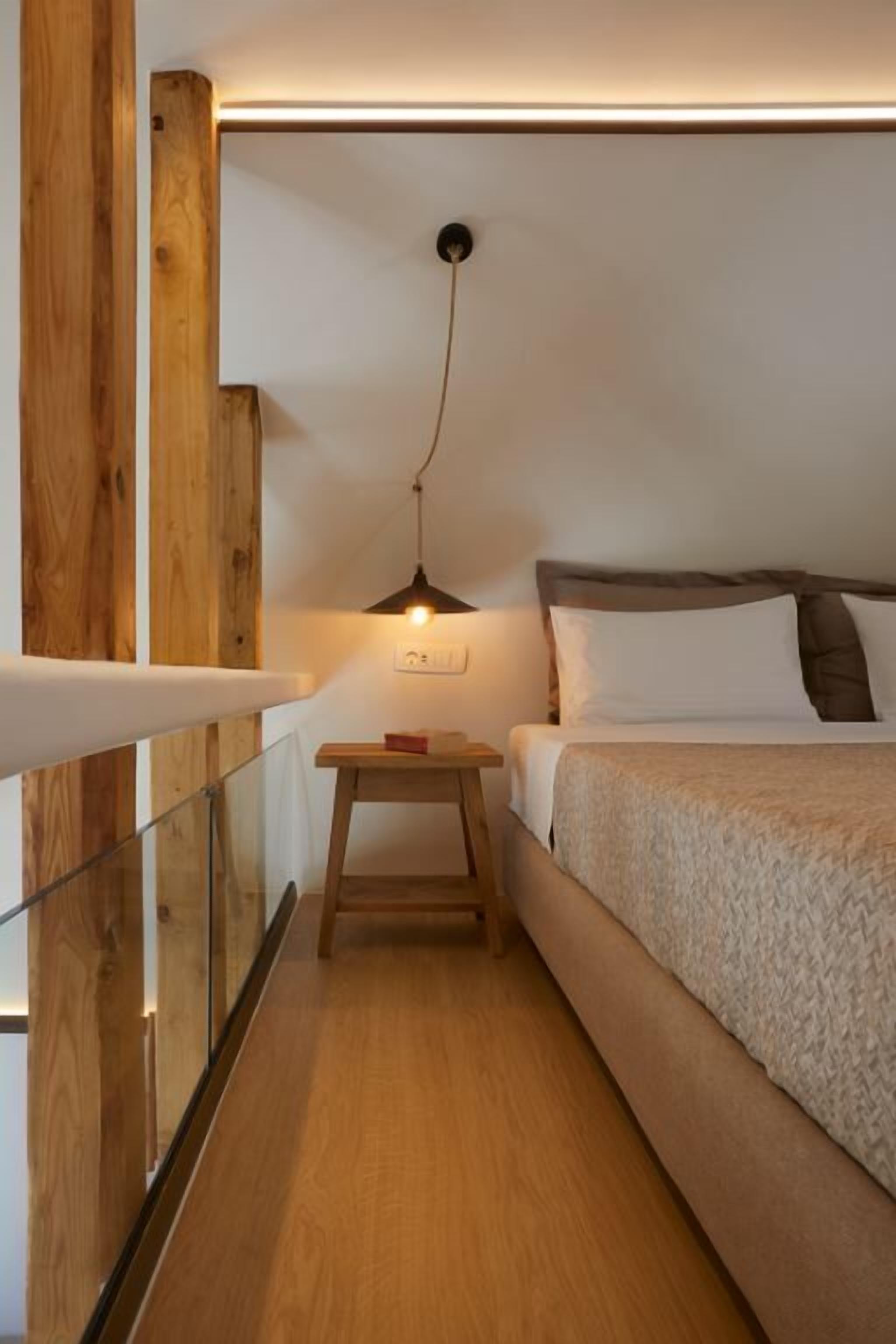 A narrow room with a bed, a small table, and a hanging light fixture.