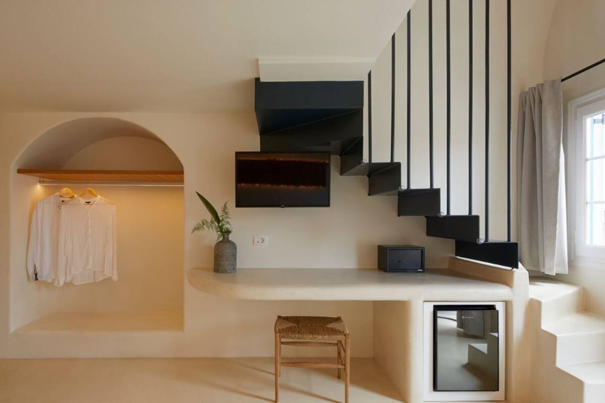 A modern interior with a staircase, a flat-screen TV mounted on the wall, a small table, and a bench.