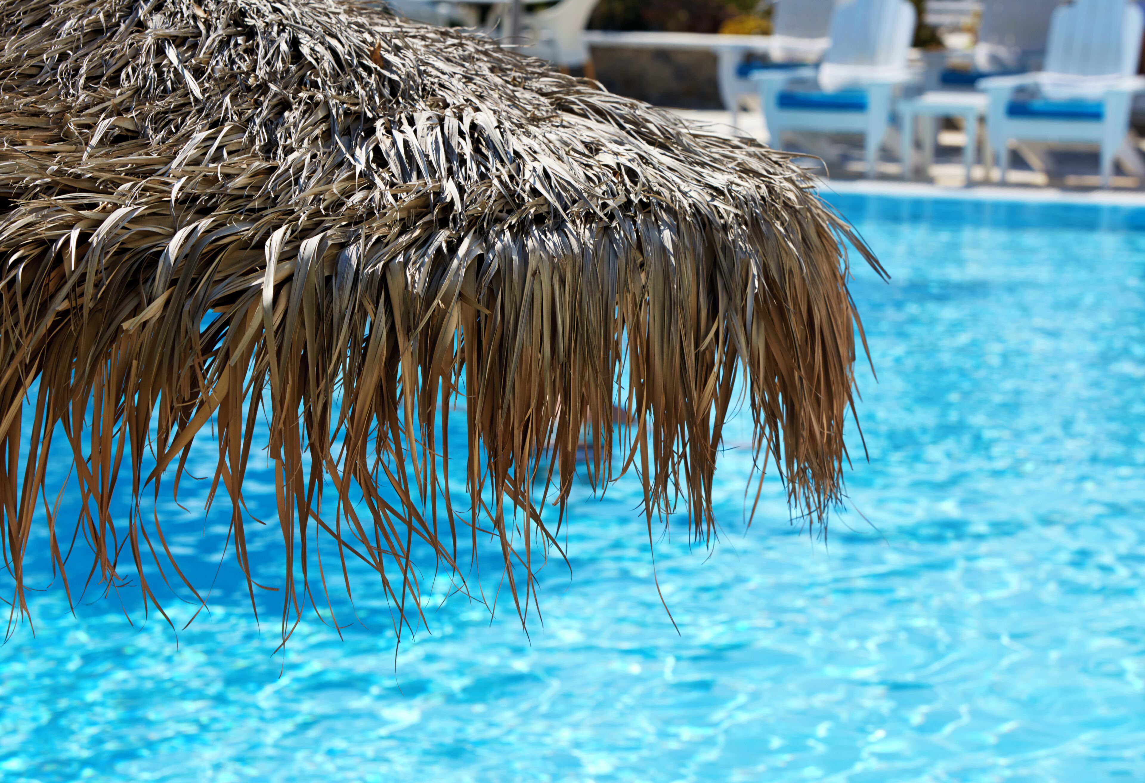 Un área de piscina con una sombrilla de paja y sillas de descanso.